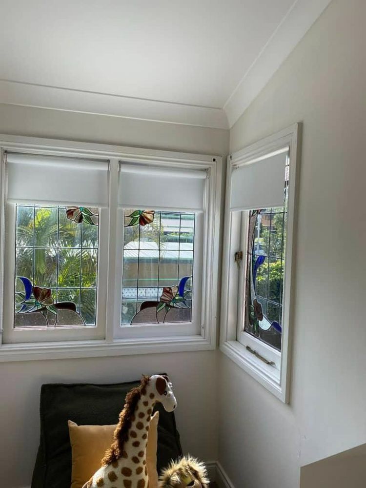 Cozy corner with three windows, a giraffe plush on a black chair, and a yellow pillow.