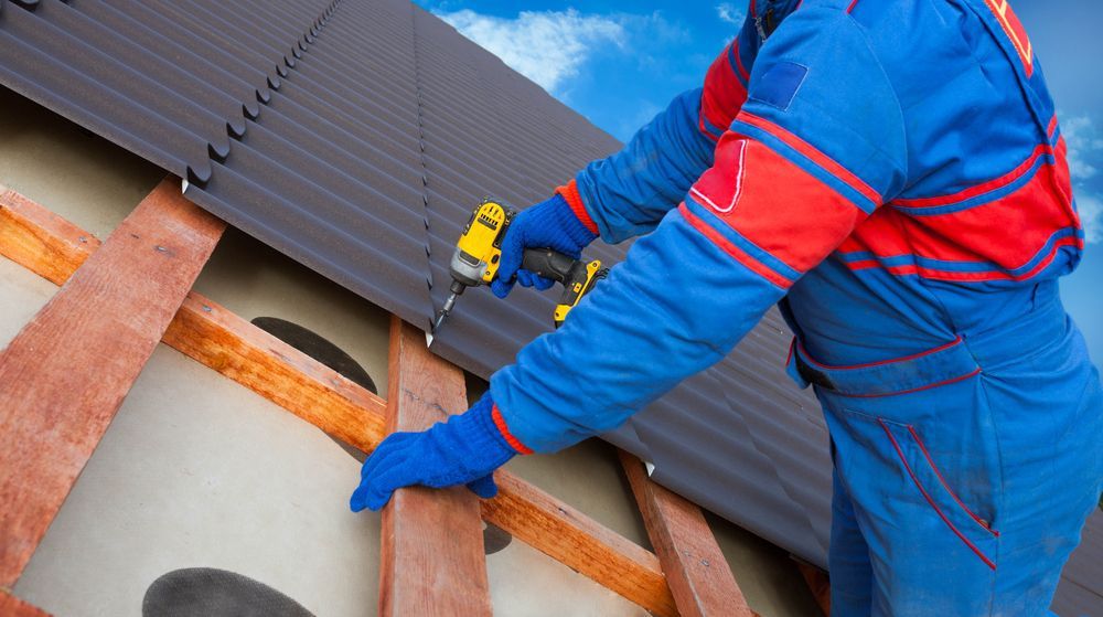 Worker In Blue and Red Uniform Securing a Roof Panel With Orange Straps and a Tool on a Slanted Roof — Geiger Solutions In Clermont, QLD