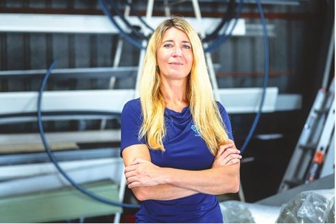 Woman with folded arms wearing a blue shirt, standing in an industrial setting.