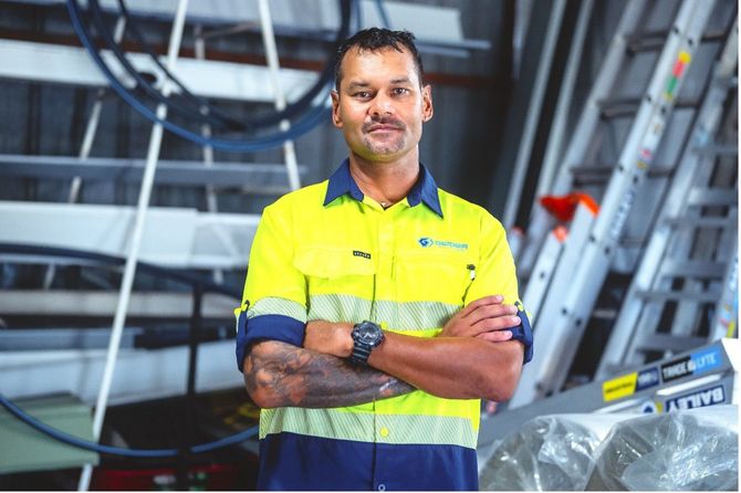 Worker in a high-visibility yellow shirt standing with arms crossed in an industrial facility