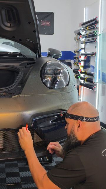 Technician working on the front bumper of a dark car in a garage