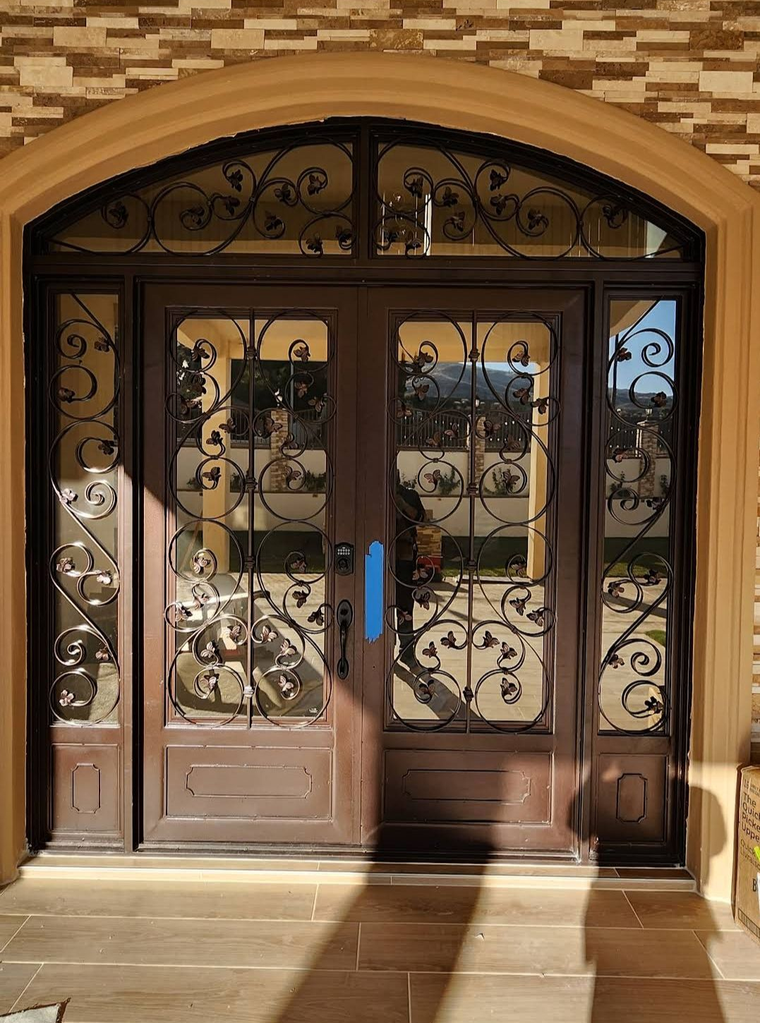 Brown arched double doors with ornate wrought-iron glass panels set in a stone entryway