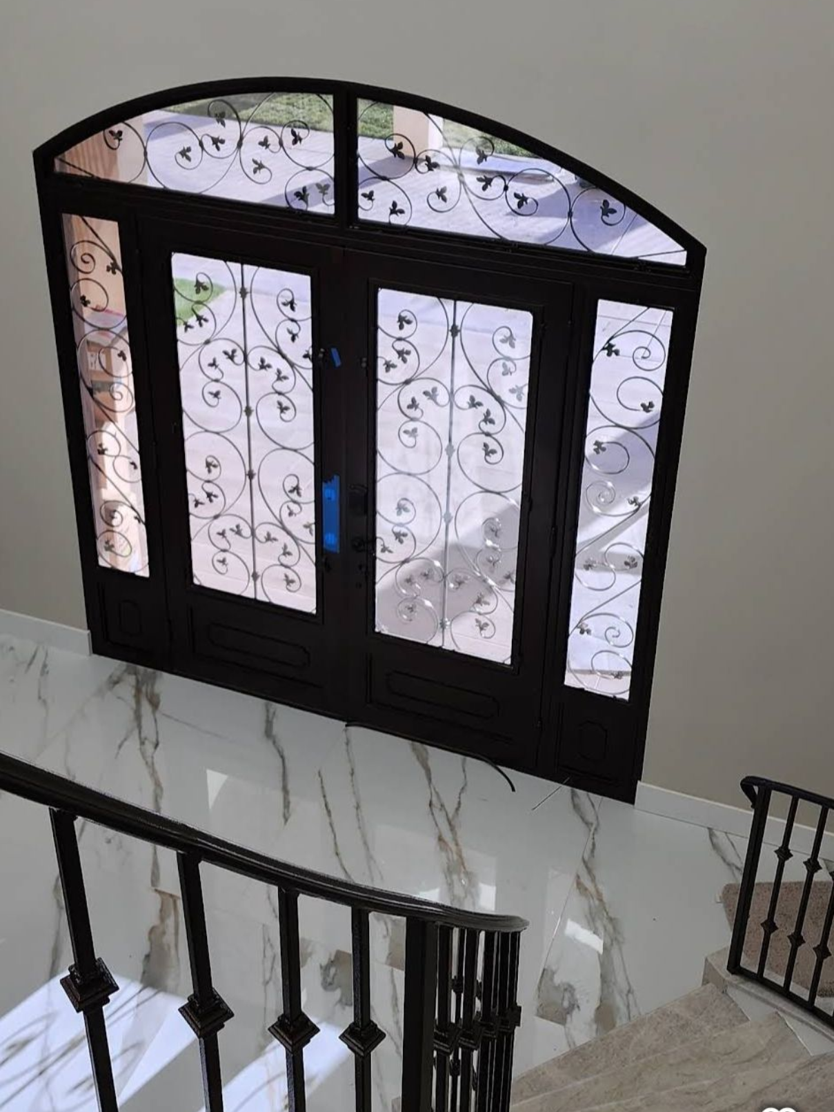 Black arched window above a staircase, with frosted glass and decorative scrollwork panels.