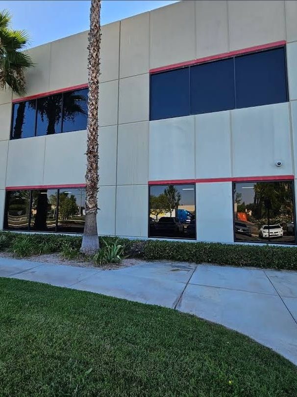 Two-story office building with reflective windows, palm tree, and sidewalk beside a grassy lawn.