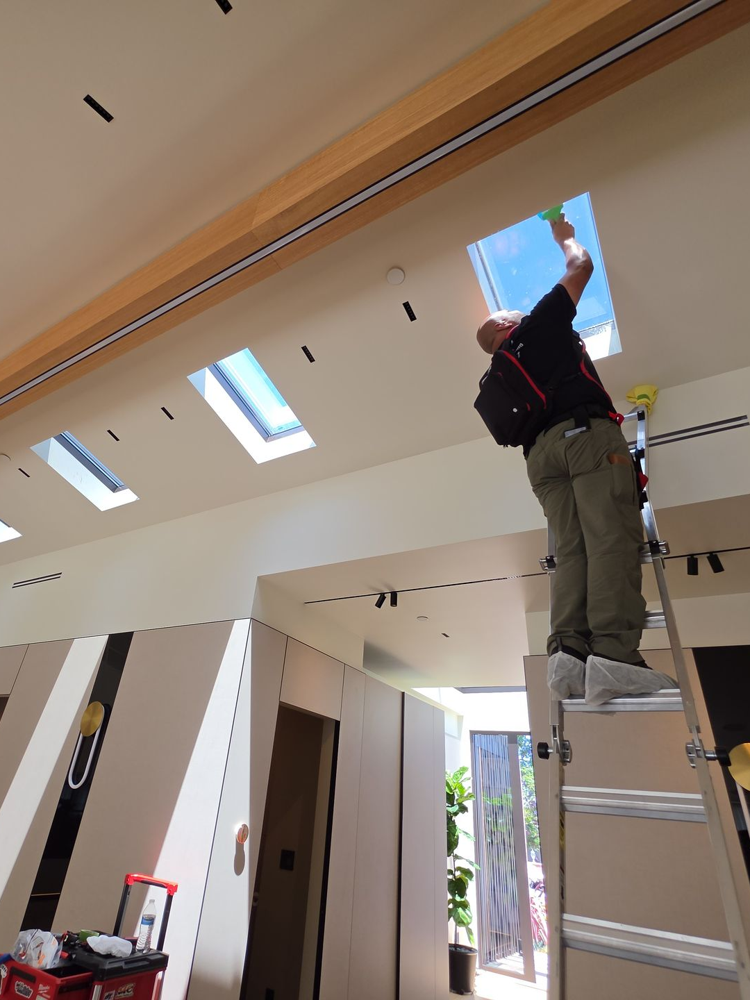 Worker standing on a ladder installing a skylight in a bright room with a high ceiling
