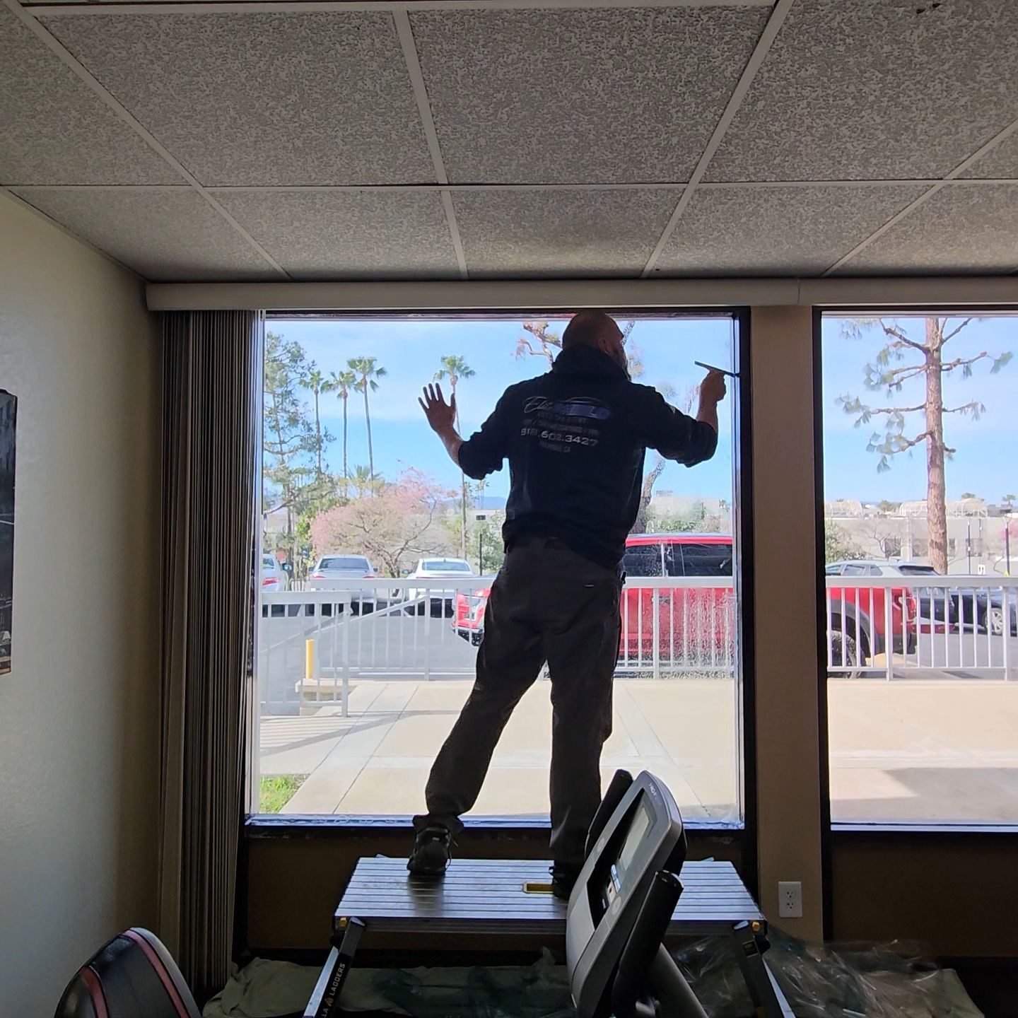 Person standing on a chair by a large window, reaching toward the glass in a room.