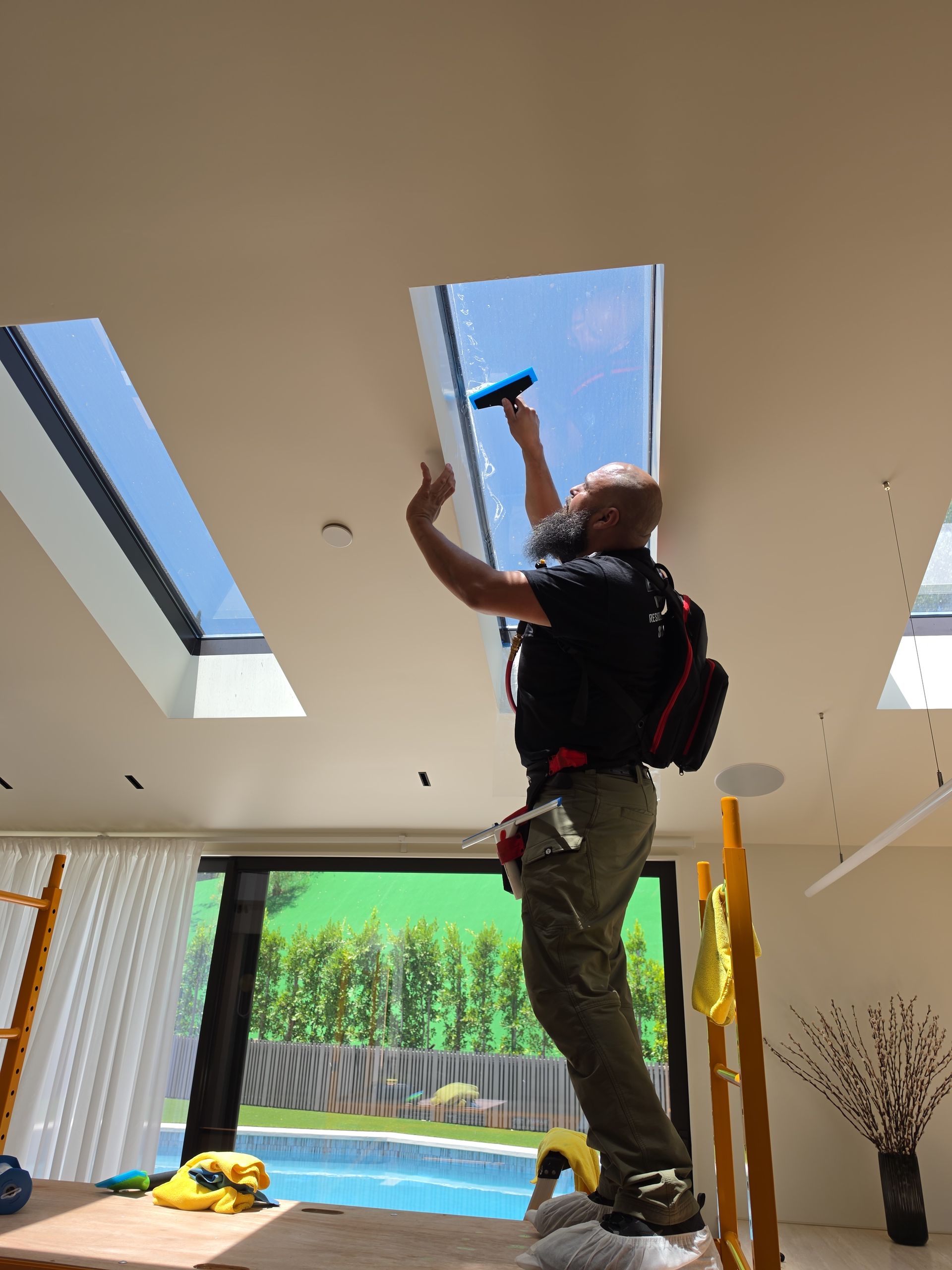 Worker installing a skylight, using a drill while standing on a ladder in a bright room