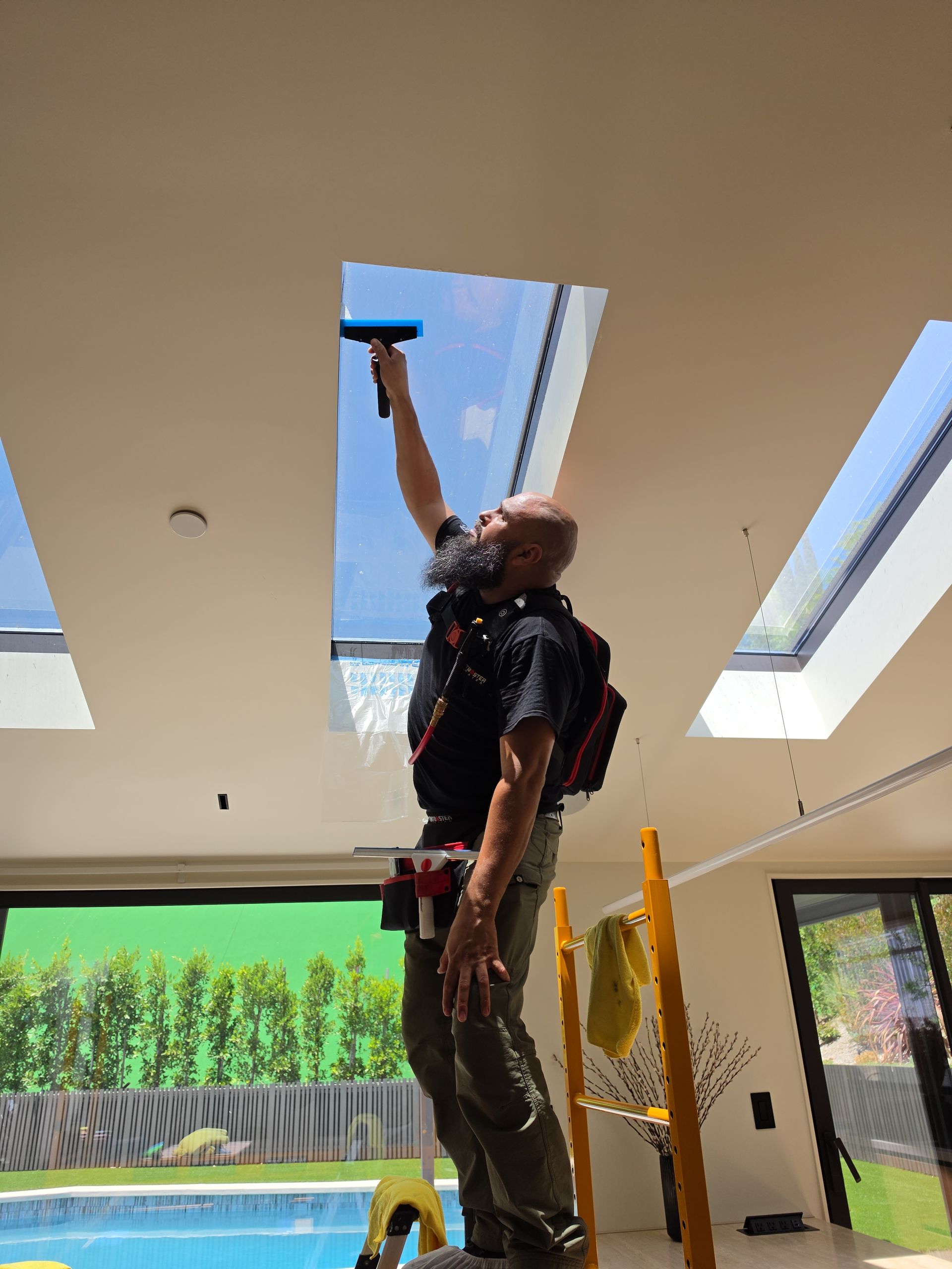 Person on a ladder cleaning a skylight indoors with a squeegee in a bright room