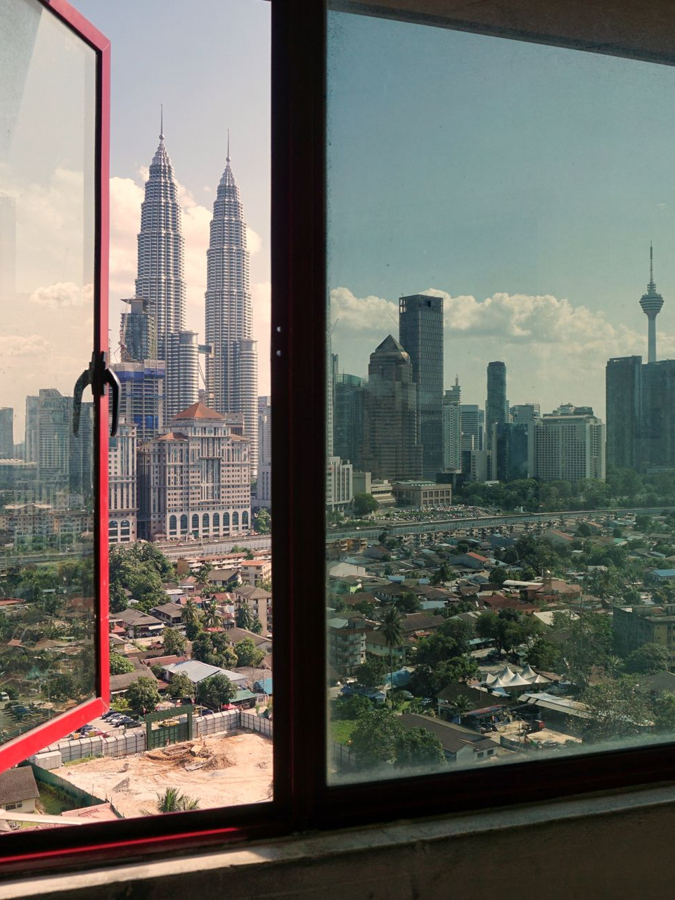 City skyline through a window, with a red-framed view of the Petronas Towers and other skyscrapers.