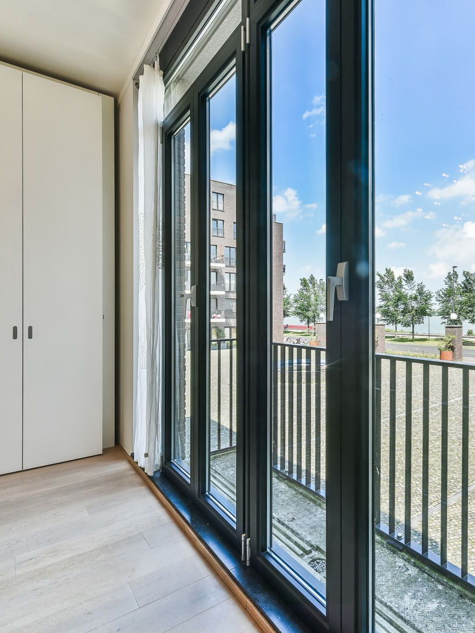 Bright room with large black-framed windows, white closet doors, and a balcony view of buildings and trees