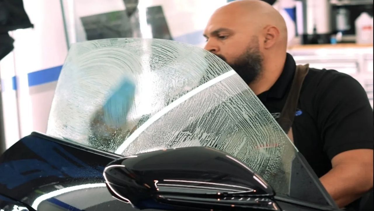A man is cleaning the windshield of a car