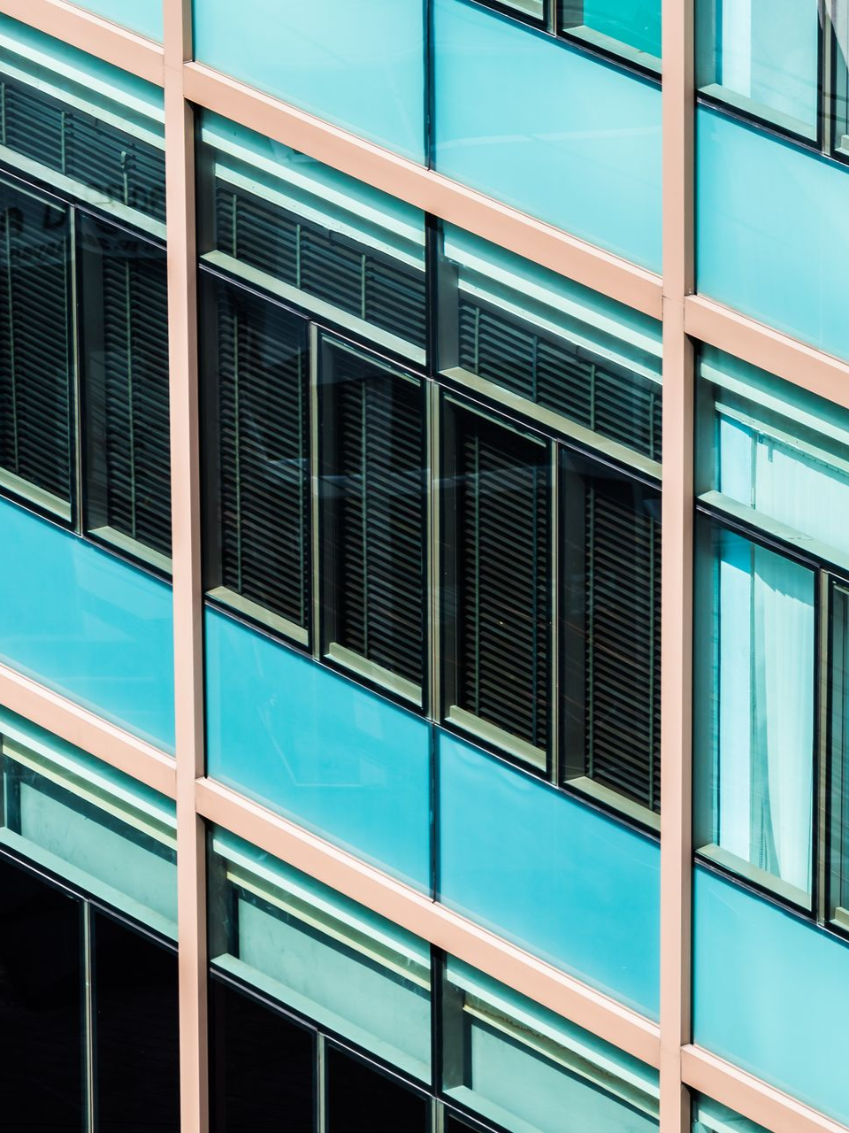 Close-up of a modern glass building facade with teal panels and black window blinds