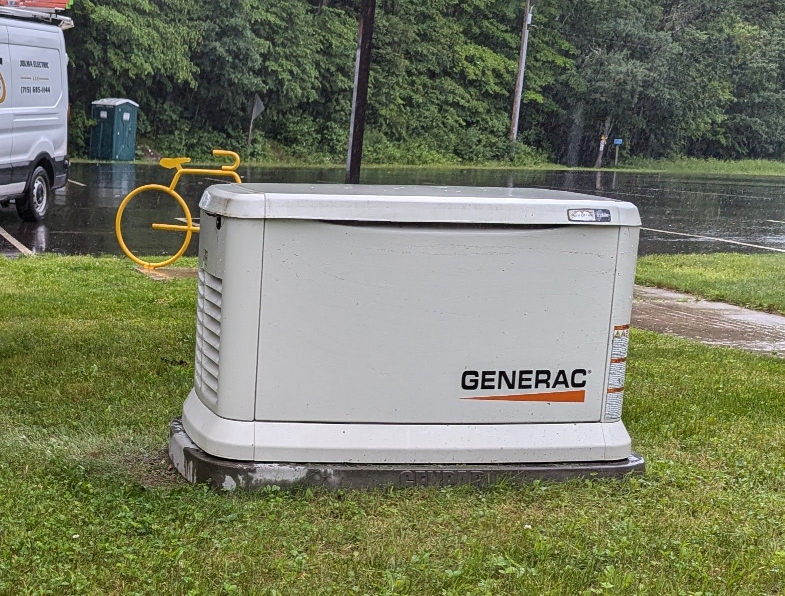 A teal industrial generator on a towable trailer parked on a city street near several cars.