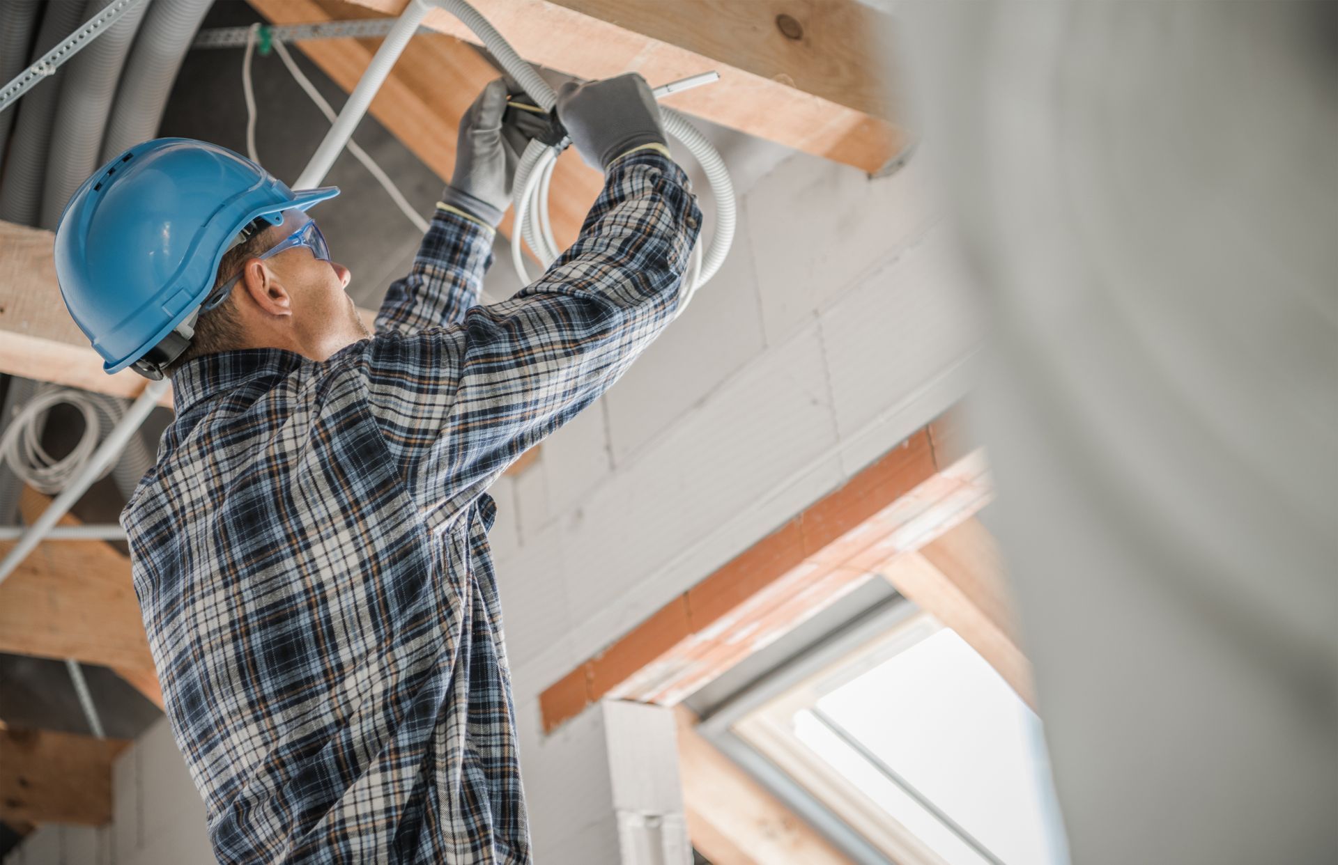 Electrician in a hard hat running ceiling conduit wiring