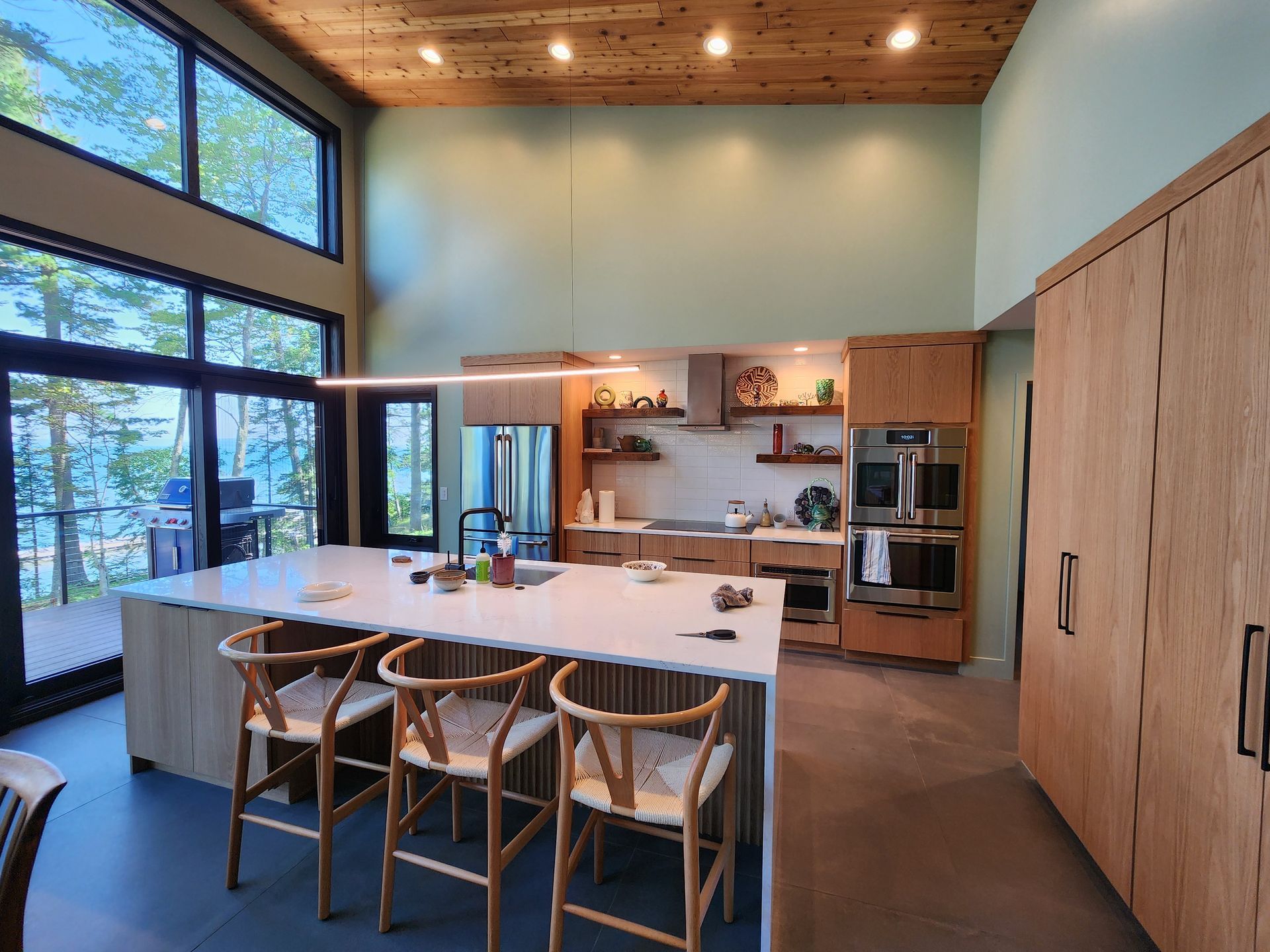 A multi-story modern rustic home at dusk, featuring a two-car garage, warm exterior lighting, and surrounding trees.