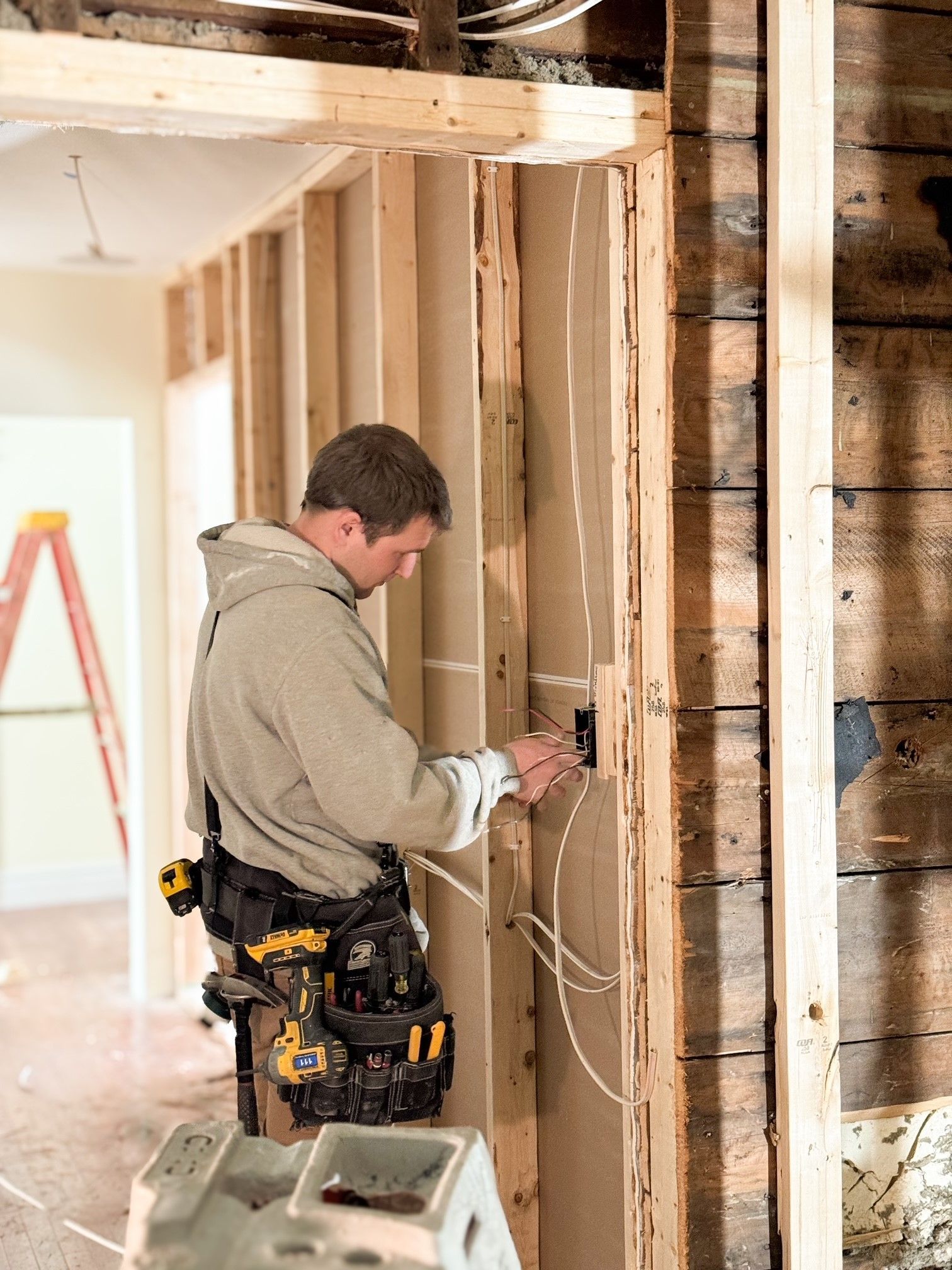 A person wearing a tool belt installs electrical wiring into a stud wall in a room under construction. A person wearing a tool belt installs electrical wiring into a stud wall in a room under construction.