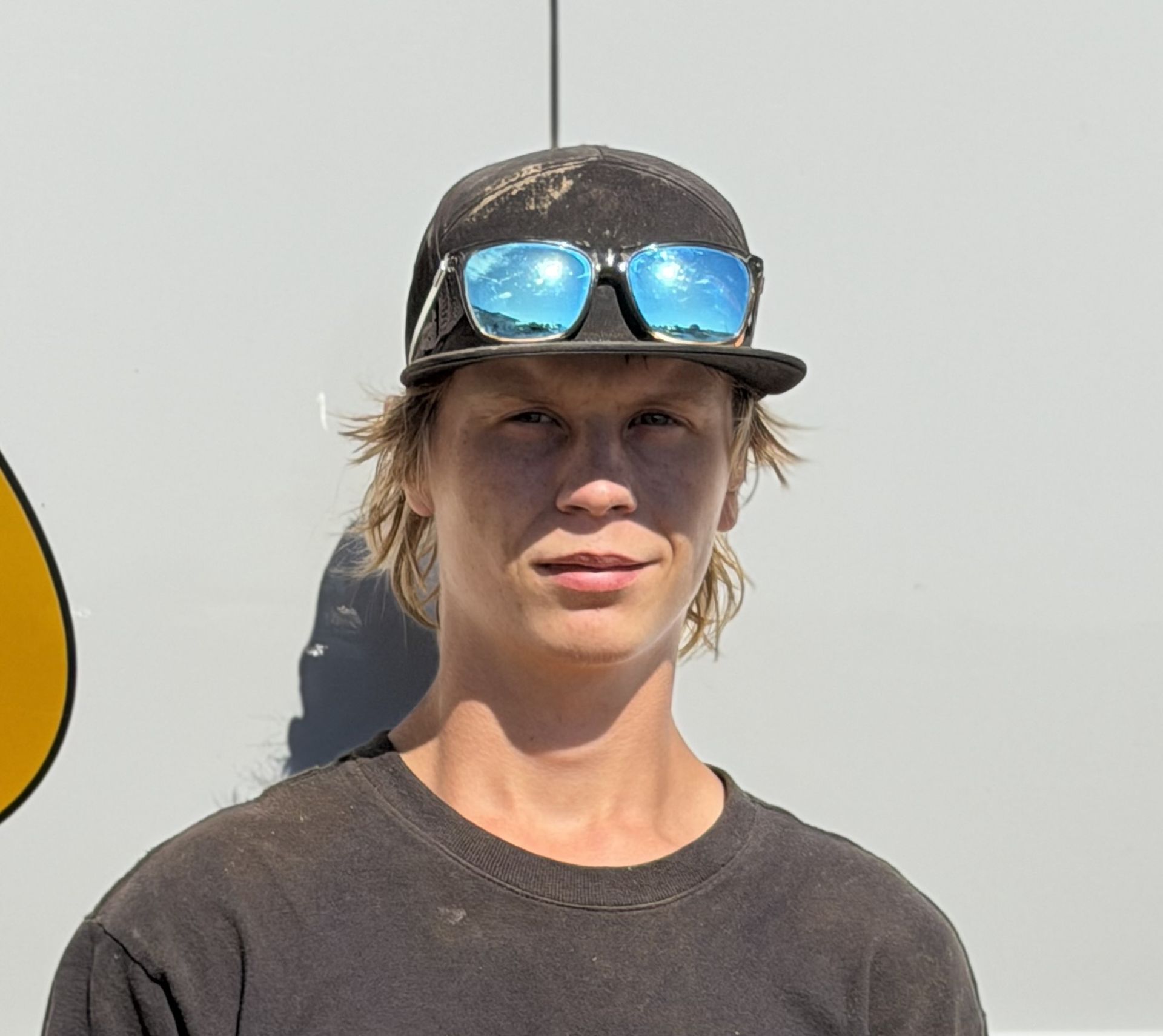 Smiling person in a gray cap and brown jacket standing in front of a vehicle logo