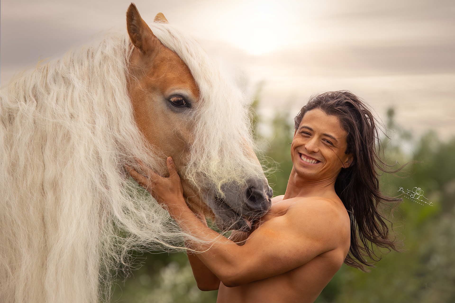Een man met lange dreadlocks glimlacht terwijl hij buiten een lichtgekleurd paard met een lange manen omarmt; er spat water op.