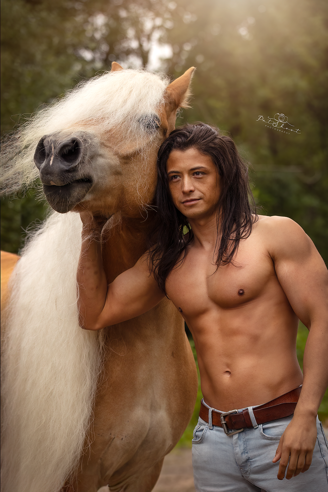 Man met lang haar, zonder shirt, poseert naast een lichtbruin paard met een lange witte manen. Buiten, zonnig weer.