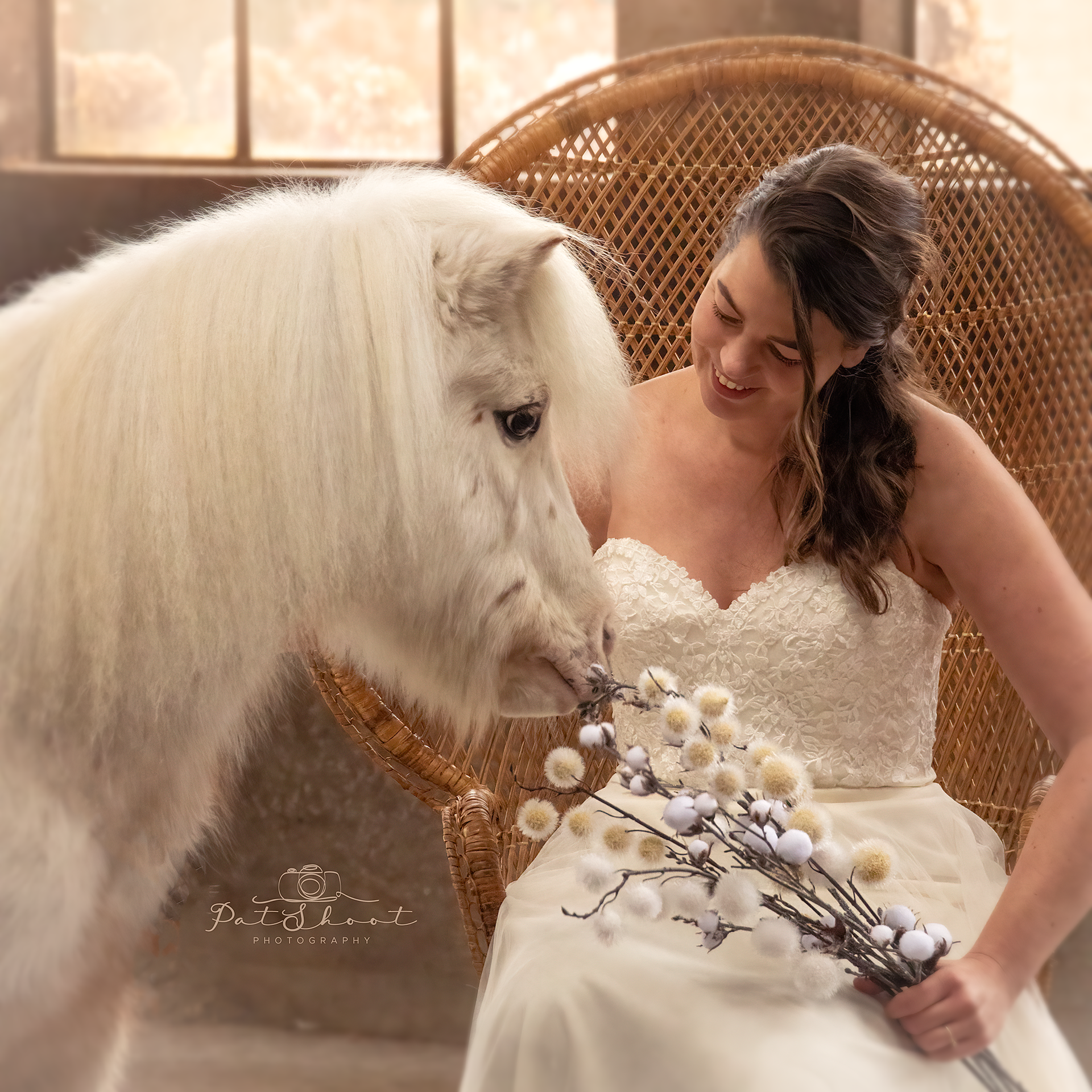 Een bruid in een witte jurk glimlacht terwijl ze een boeket vasthoudt; een witte pony snuffelt aan de bloemen binnen.