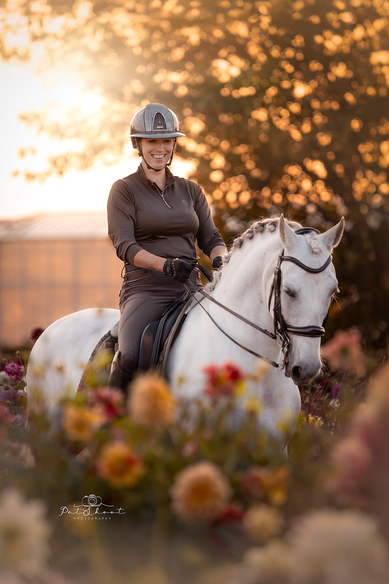 Vrouw op een wit paard, met helm op, in een bloemenveld bij zonsondergang.