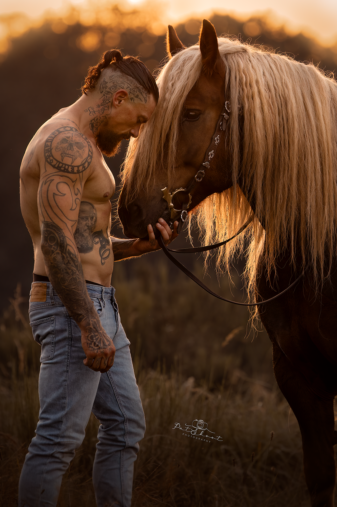 Een man met tatoeages leunt met zijn hoofd tegen het hoofd van een paard in het warme, gouden licht.