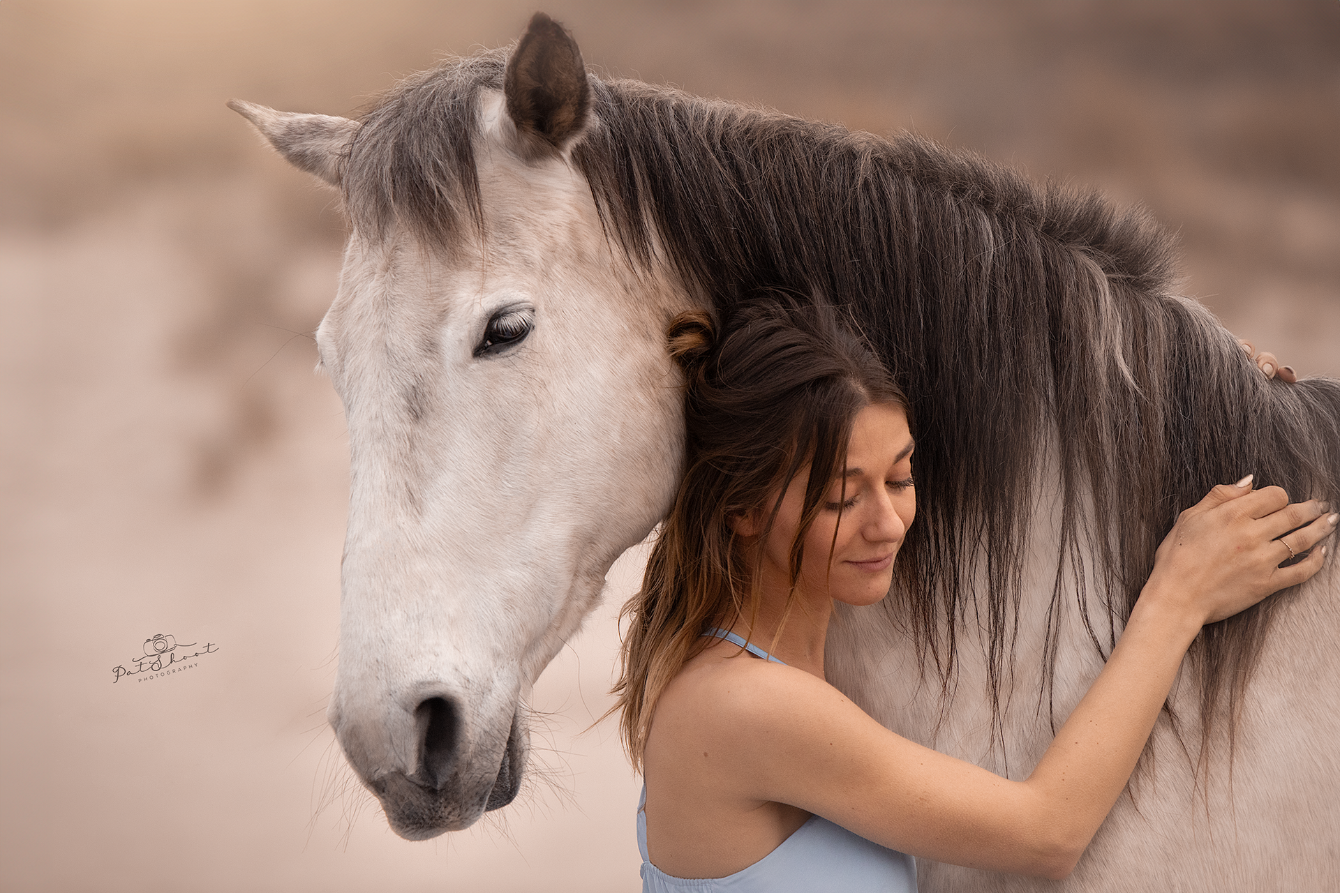 Een vrouw omhelst een wit paard; beiden kijken naar beneden en lijken tevreden.