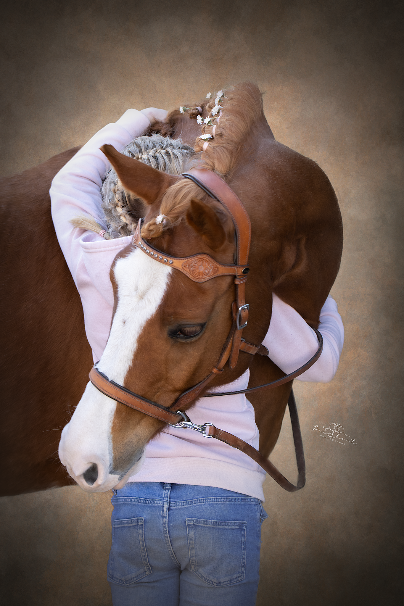Persoon die een bruin paard met een witte bles en een wit hoofdstel omarmt; lichtroze shirt en blauwe spijkerbroek.