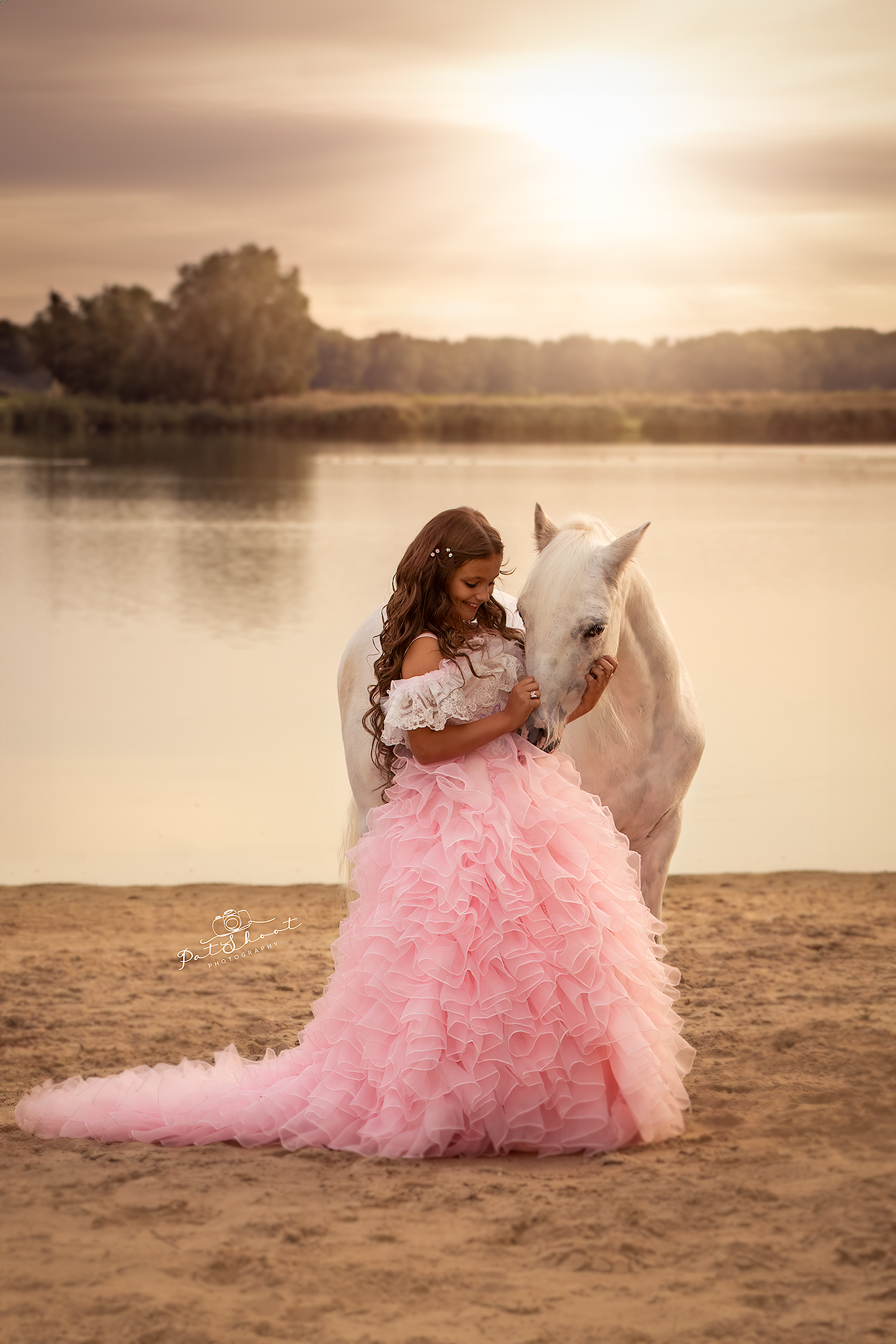 Magische fotoshoot op Locatie Vrouw in roze jurk die een wit paard omarmt op een zandstrand bij zonsondergang.