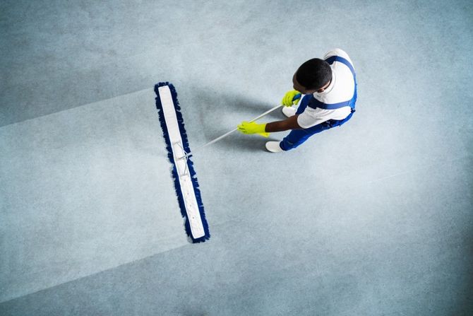 Top-down view of a person in blue and white using a yellow squeegee on a smooth floor