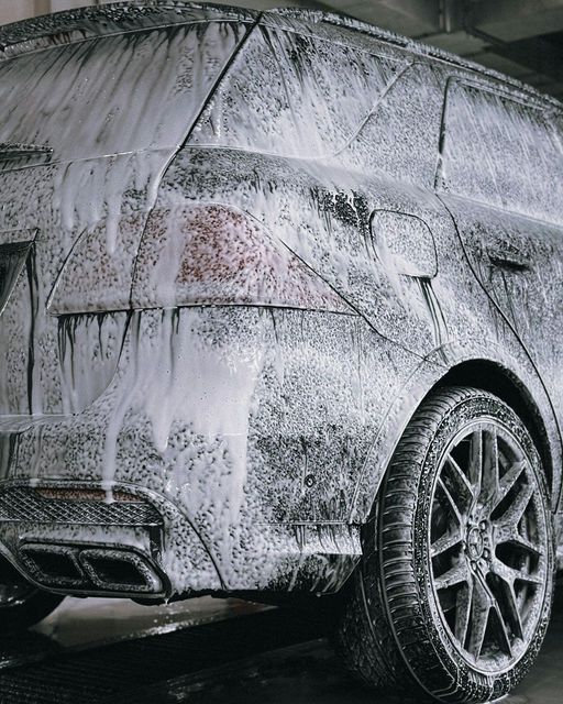 Car covered in white foam at a car wash. Rear of the vehicle is visible with taillights and a tire.