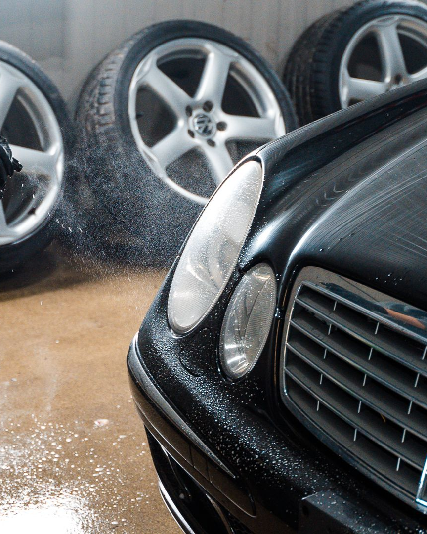 A person is using a blue squeegee to remove plastic from the hood of a car