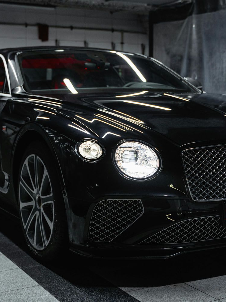 Black luxury sedan parked in a dim garage, front view with headlights on