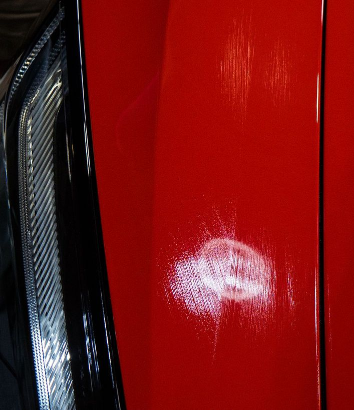 Close-up of a glossy red car panel with a white scratch or paint scuff