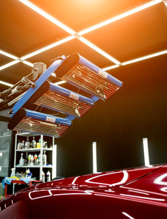 Robot arm polishing a red car hood under bright orange workshop lights