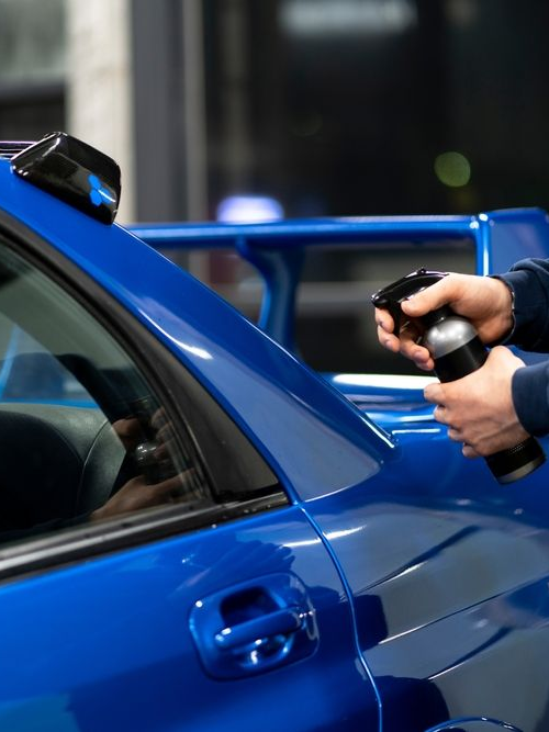 Person holding a tool to the side of a blue car at a service station