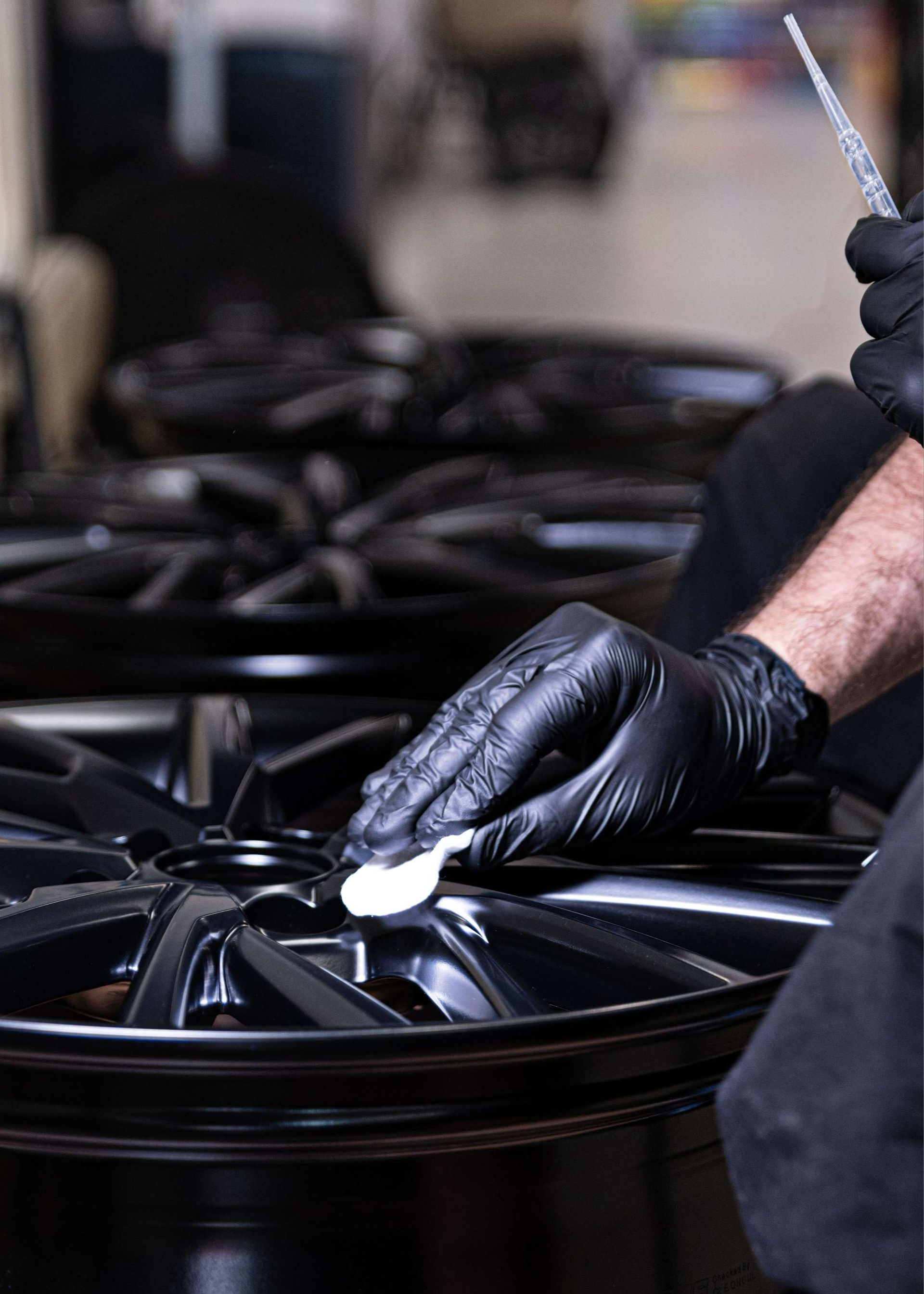 Gloved hands polishing a black alloy wheel with a cloth in an auto shop