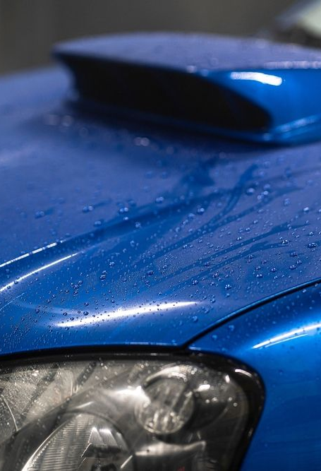 Blue car hood and headlight close-up with water droplets
