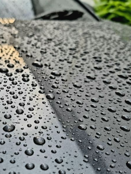Raindrops on a dark car roof, close-up