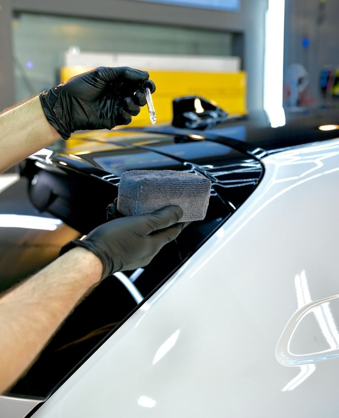 Gloved hands applying black vinyl wrap to a glossy white car hood.