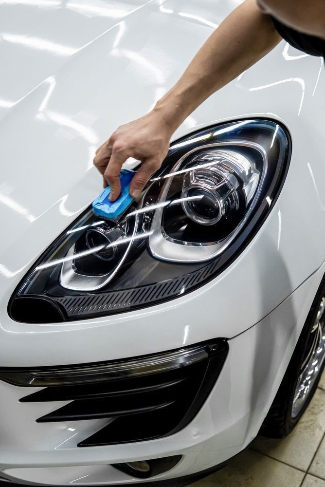 Hand cleaning a white car’s headlight with a blue cloth