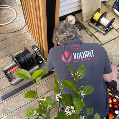 A man wearing a valiant electrical shirt is working on a deck. A man wearing a valiant electrical shirt is working on a deck.