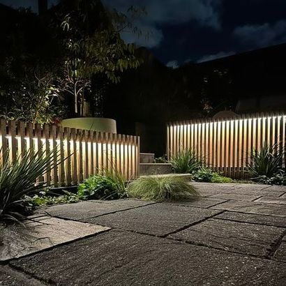 A wooden fence is lit up at night in a backyard. A wooden fence is lit up at night in a backyard.