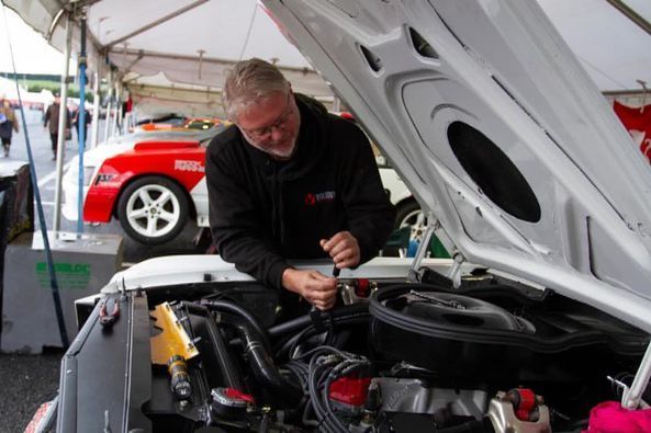A man is working on the engine of a white car