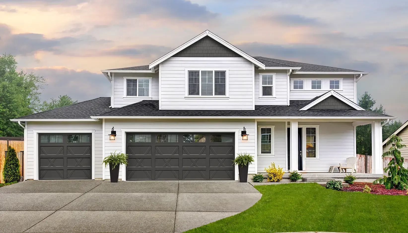 A two-story house with white siding, dark gray accents, a double garage, and a manicured lawn under a cloudy sky.