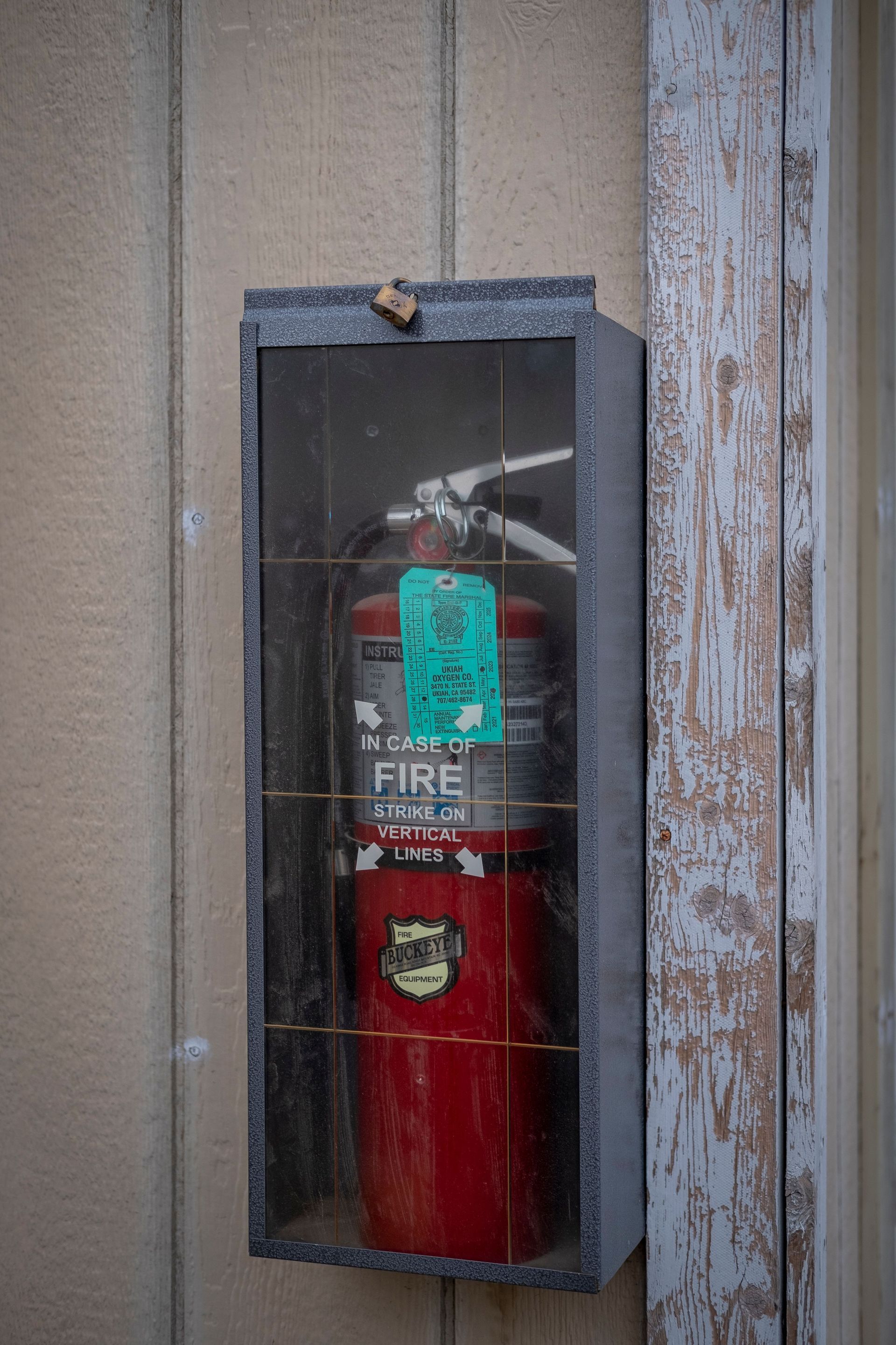 Red fire extinguisher in a glass wall cabinet behind worn gray door trim.