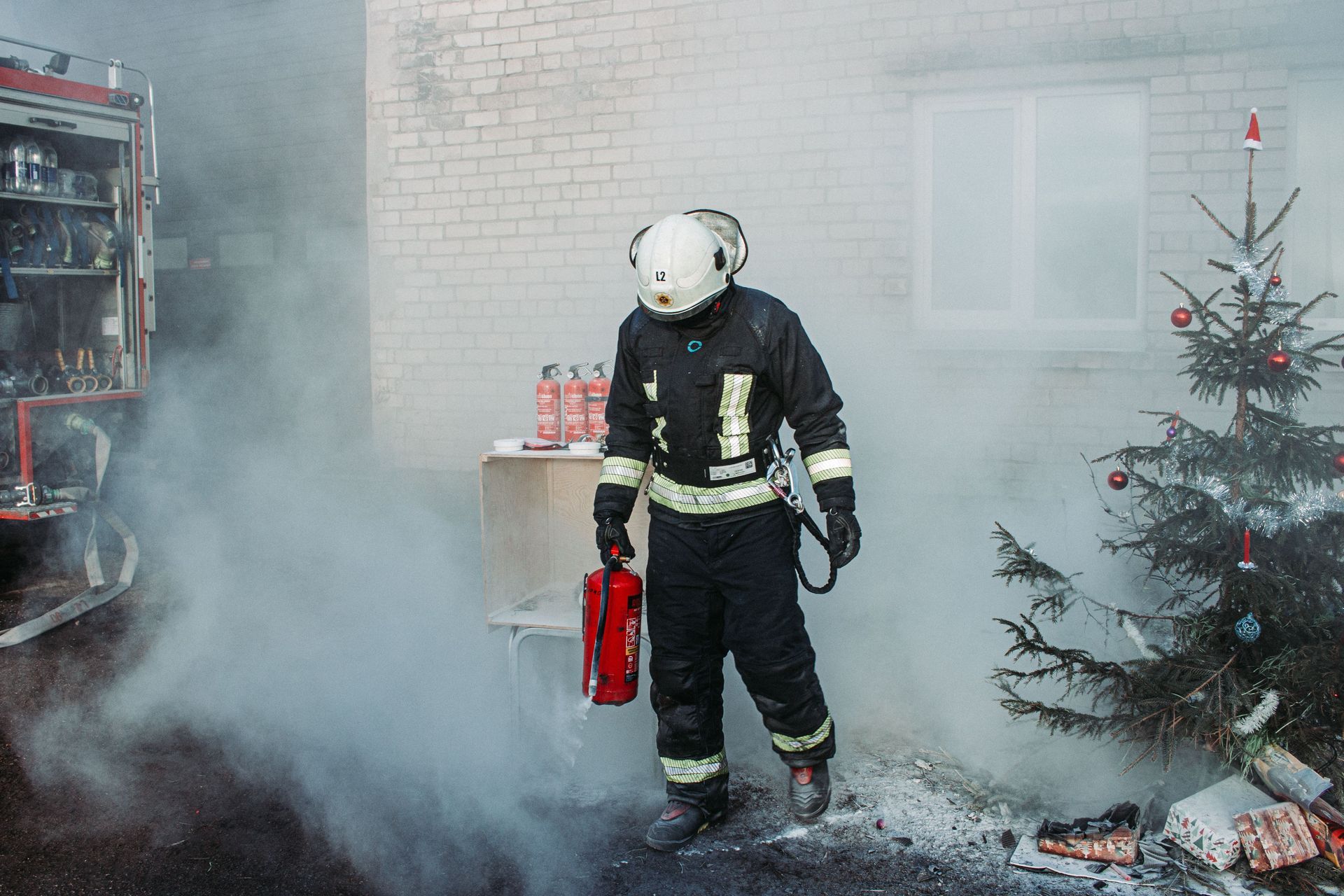 Firefighter carrying extinguisher amid heavy smoke in a room, with a small Christmas tree nearby