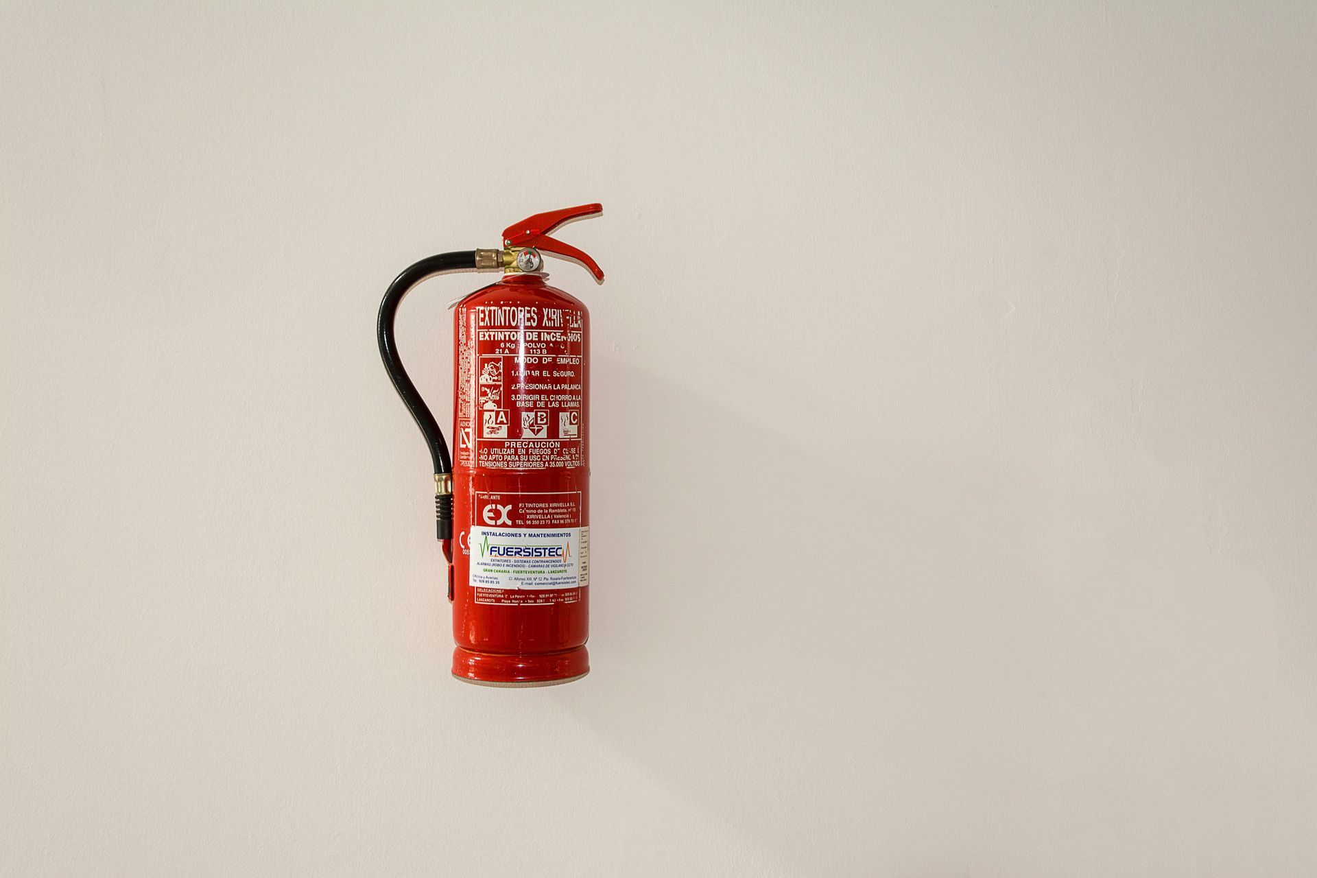 Red fire extinguisher mounted on a plain beige wall