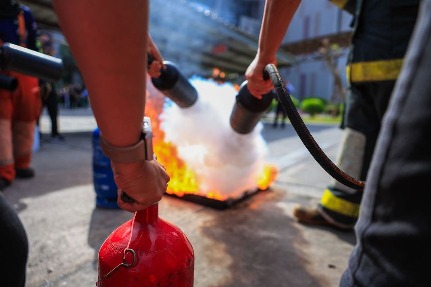 Firefighters aim hoses at a blaze in a street, with water spraying toward bright flames.