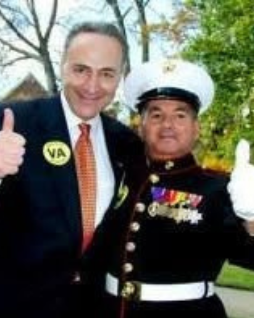 Man in suit and Marine in uniform giving thumbs up. VA pin visible. Outdoors.